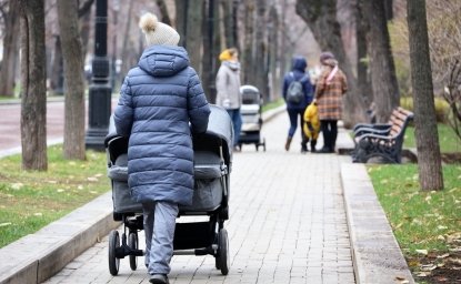 Mothers walking with baby prams on city street at autumn. Woman with stroller for twins in foreground