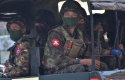 Soldiers in uniforms and masks sitting on a truck.