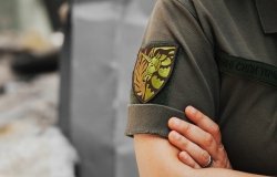 Ukrainian military woman with the lgbt chevron in her hands on the background of an exploded house